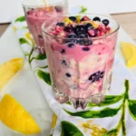 Two lemon berry overnight oats with kefir in glasses on a lemon towel on a kitchen counter.