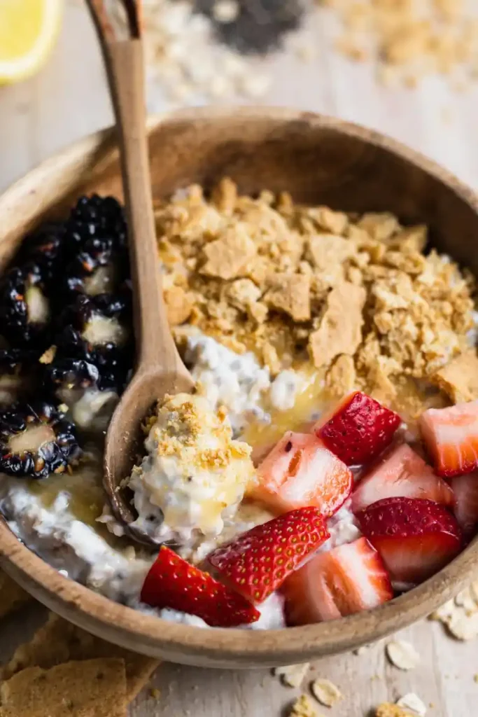 Lemon cheesecake overnight oats in a wooden bowl with a wooden spoon in it.