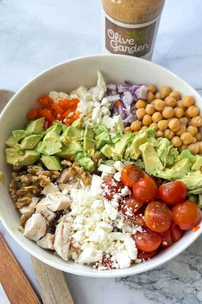 A birds-eye view of a Mediterranean chicken salad in a bowl next to a bottle of Olive Garden dressing.