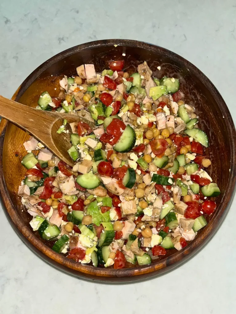 Mixing the ingredients of the Mediterranean salad in a wooden bowl with a spoon.