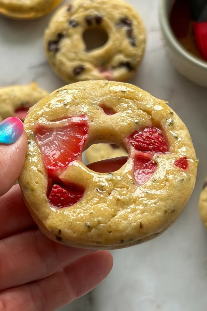 Someone holding up a pancake donut that has been dipped in maple syrup.
