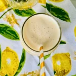 A birds-eye view of a glass of creamy peach pineapple smoothie made with kefir on a lemon decorated towel.
