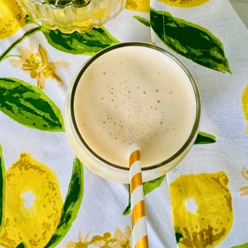 A birds-eye view of a glass of creamy peach pineapple smoothie made with kefir on a lemon decorated towel.