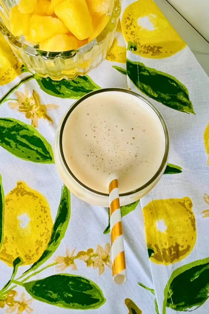 A birds-eye view of a glass of creamy peach pineapple smoothie made with kefir on a lemon decorated towel.