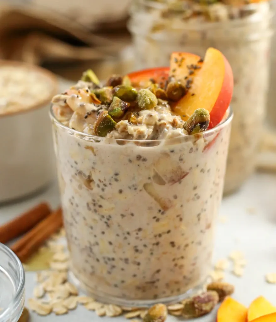 Overnight oats in a clear glass topped with fresh peaches on a table.
