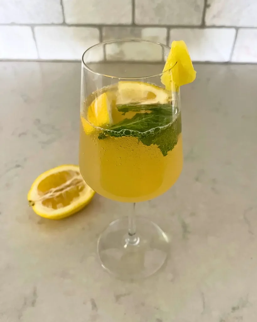 A pineapple lemon kombucha spritzer in a wine glass on a counter.