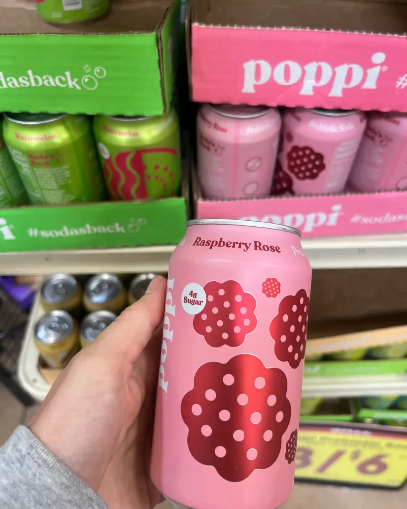 Someone holding a can of the prebiotic drink Poppi with cans of it in the background.