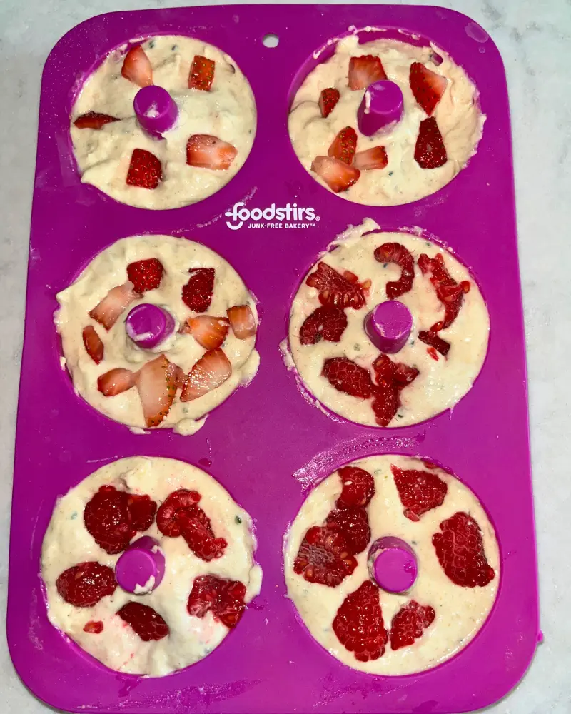 The donut batter in the molds with sliced strawberries and raspberries on top.