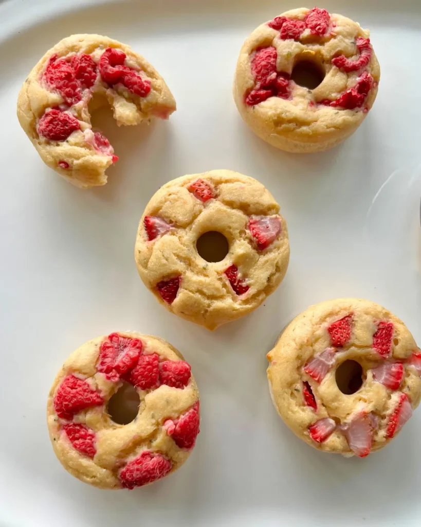5 protein donuts with strawberries and raspberries in them on a white platter.