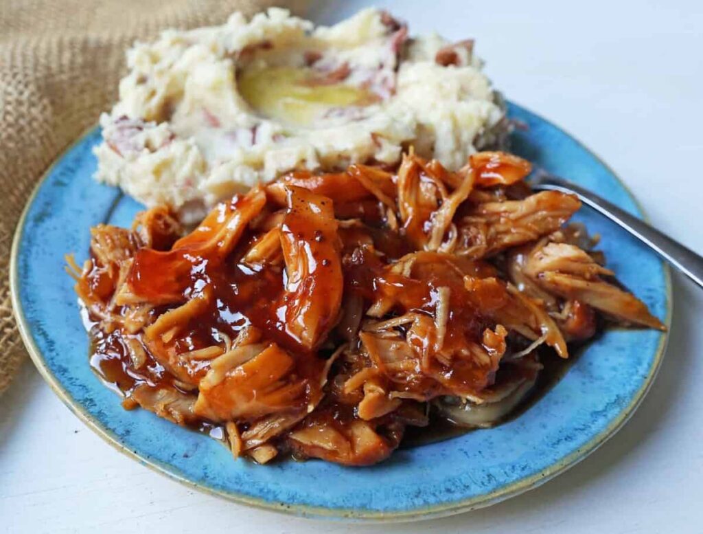 Slow cooker peach barbecue sauce chicken on a plate next to mashed potatoes.