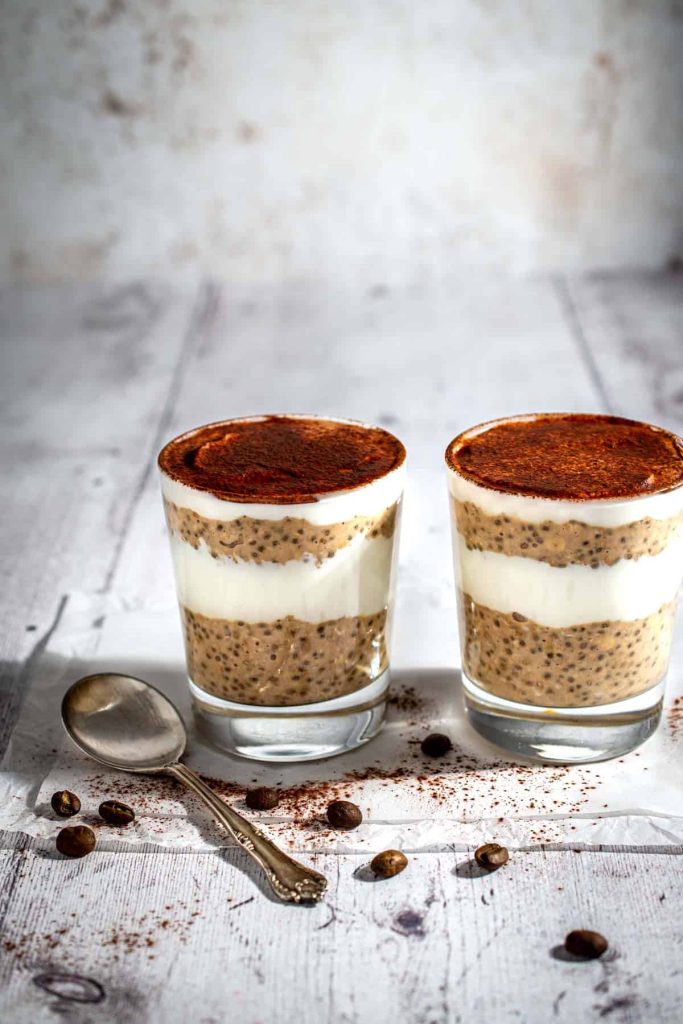 Two glass jars of tiramisu overnight oats on a table next to a spoon.