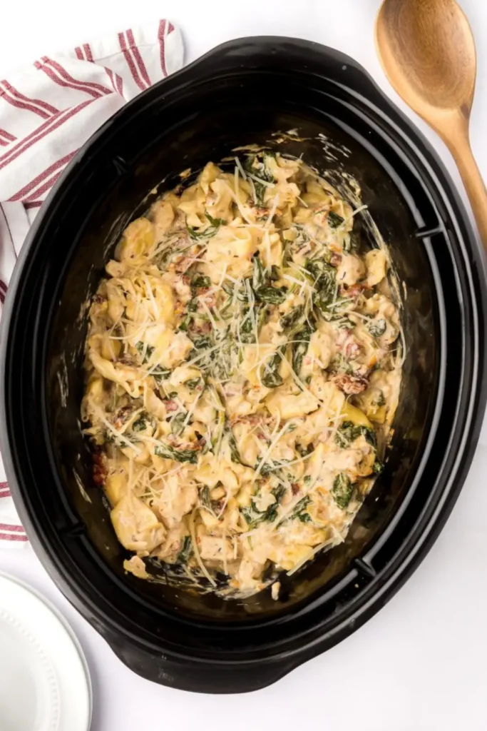 Tuscan chicken and tortellini cooking in a crockpot on a kitchen counter.