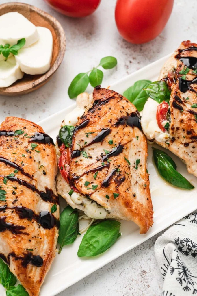 Baked Caprese chicken on a white platter garnished with basil.