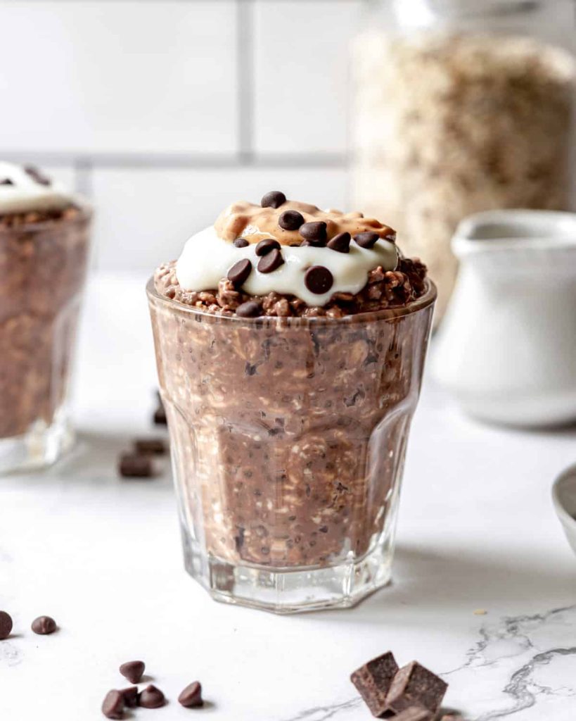 Chocolate peanut butter overnight oats topped with mini chocolate chips in a large clear glass.