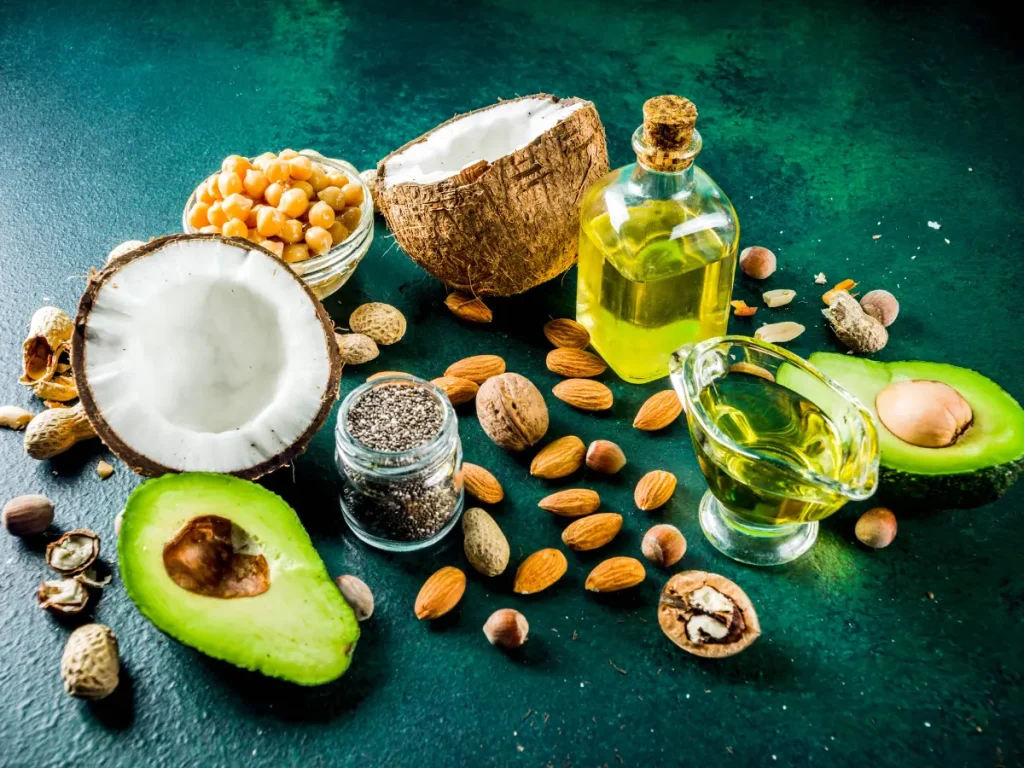 Olive oil, avocados, coconuts, nuts and seeds on a counter to represent healthy fats.