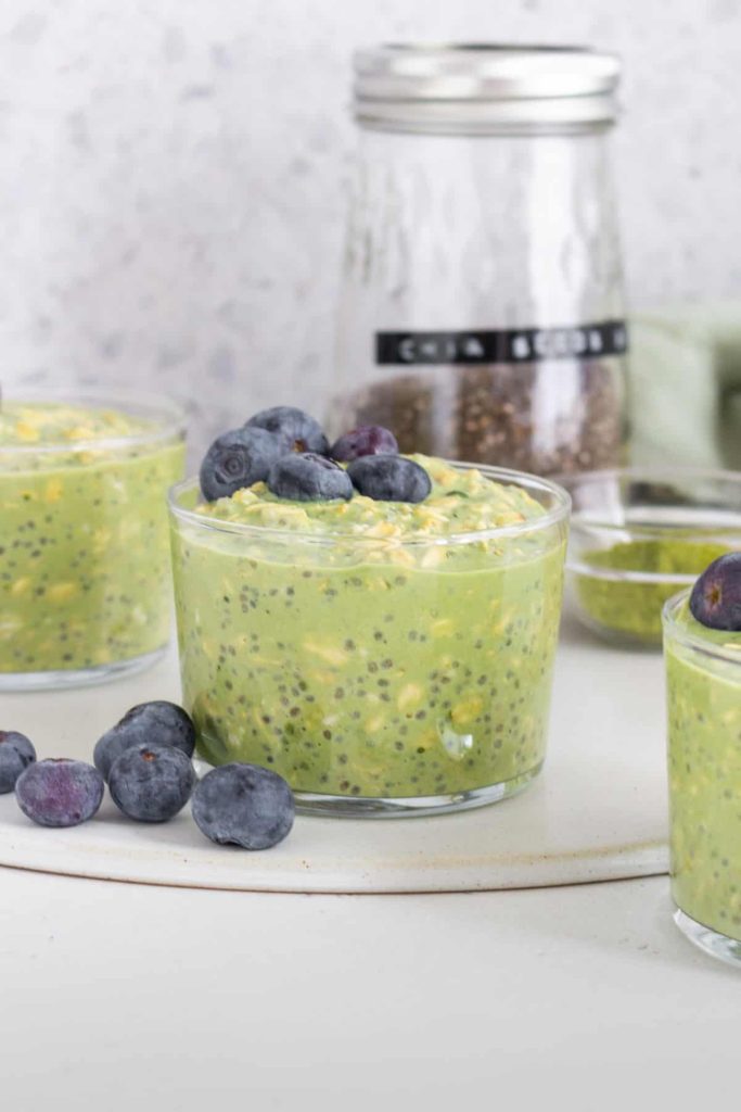 Matcha overnight oats topped with blueberries on a counter surrounded by more glasses of overnight oats.