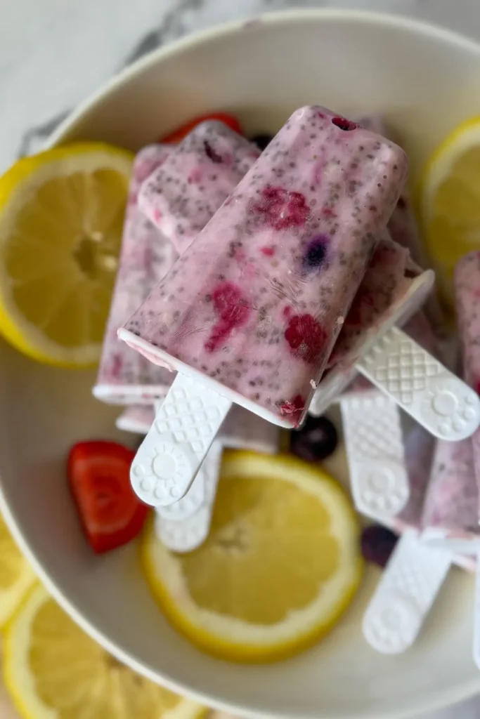 A birds-eye view of lemon berry popsicles on a white plate with lemon wedges and berries.