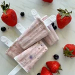 4 lemon berry protein popsicles stacked on top of each other on a counter garnished with berries.