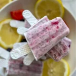 A birds-eye view of a plate with lemon berry popsicles stack on top of one another next to lemon wedges and berries.