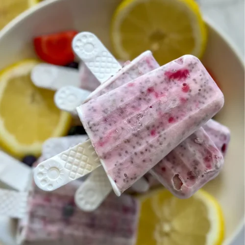 A birds-eye view of a plate with lemon berry popsicles stack on top of one another next to lemon wedges and berries.