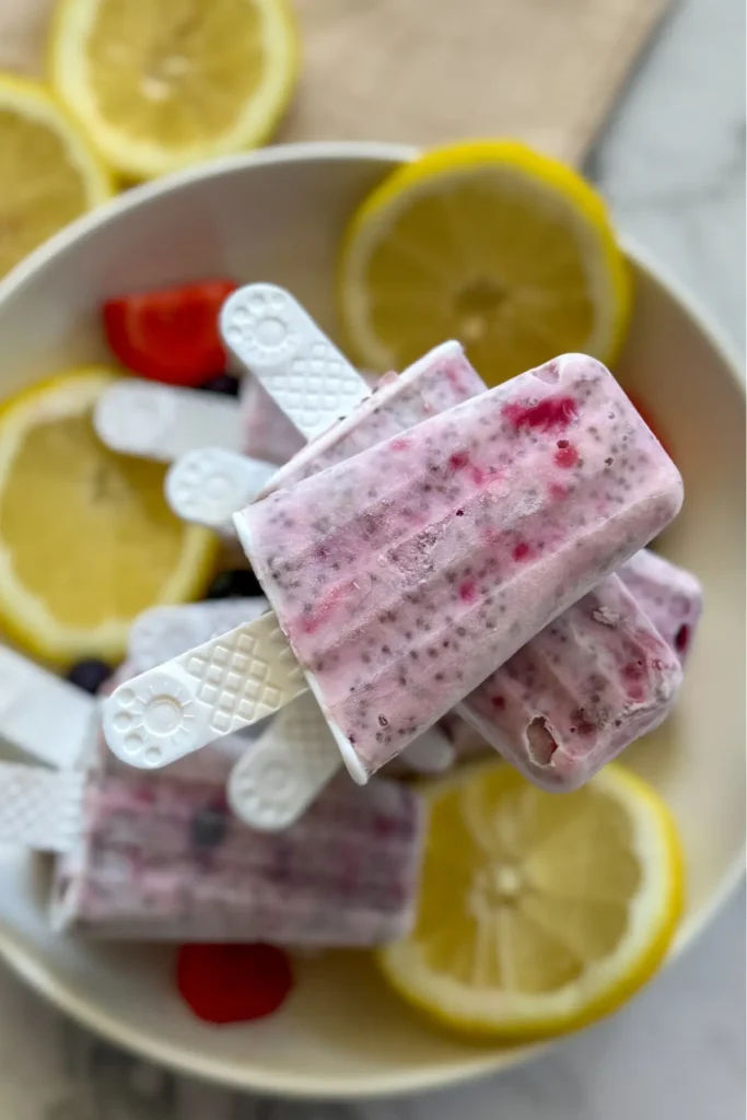 A birds-eye view of a plate with lemon berry popsicles stack on top of one another next to lemon wedges and berries.
