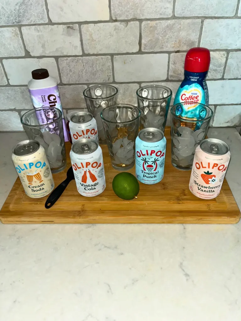 A wooden cutting board full of glasses of ice, coffee creamer, and Olipop sodas.