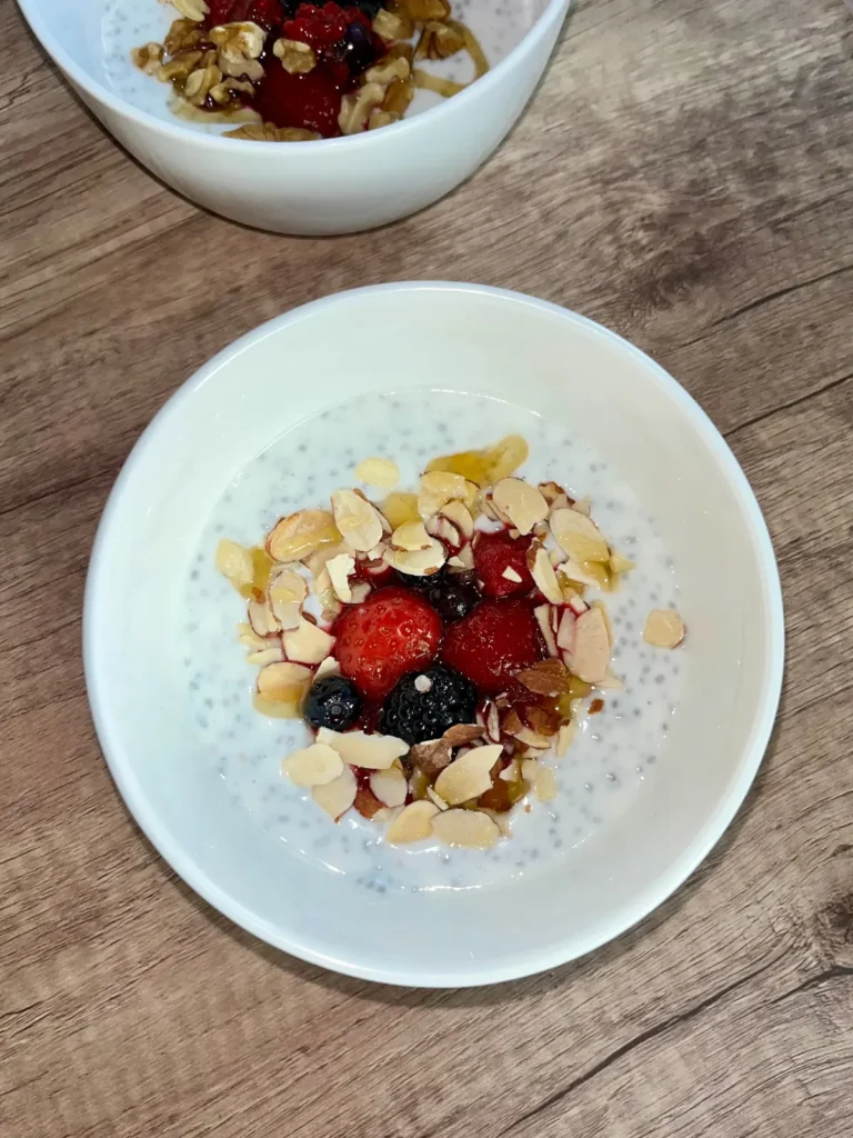 A chia breakfast bowl topped with sliced almonds and mixed berries on a wooden counter.
