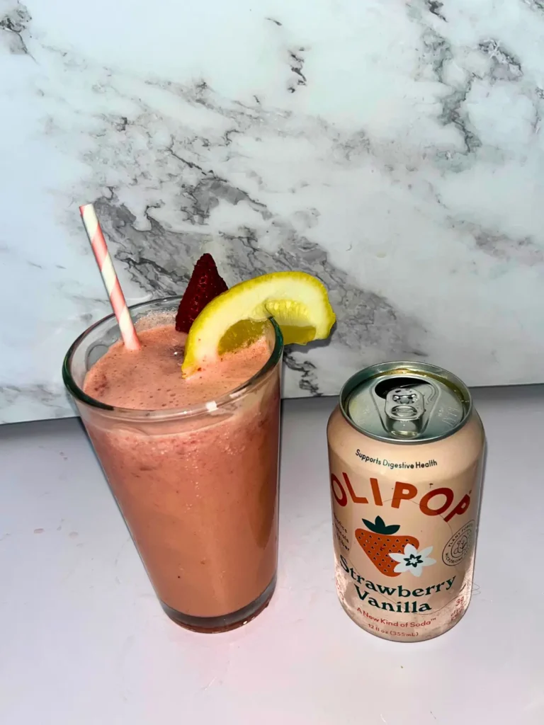 An Olipop dirty soda with strawberries and cream in a large glass next to a can of Olipop.