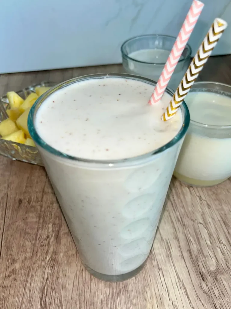 A thick and creamy pineapple protein smoothie with kombucha in a glass with two straws in it.