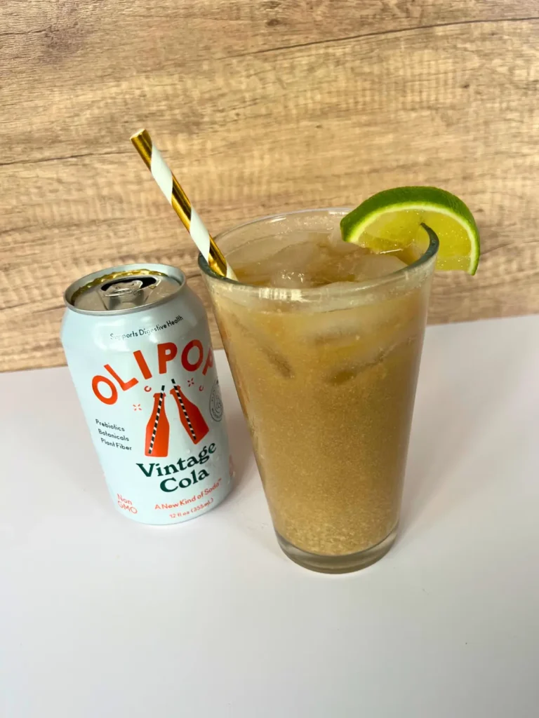 A traditional dirty soda in a large glass garnished with a lime next to a can of Vintage Cola Olipop.