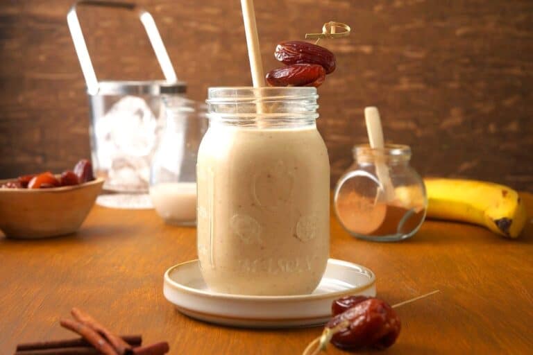 A creamy date smoothie in a glass jar with a straw in it on a table.