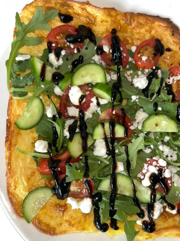 A cottage cheese flatbread with arugula, chopped cucumber, diced tomatoes, goat cheese, and a drizzle of balsamic glaze on top.