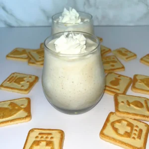 Two small glasses of Chessmen cookie banana protein pudding on a counter surrounded by Chessmen cookies.