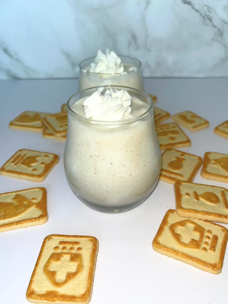 Two small glasses of Chessmen cookie banana protein pudding on a counter surrounded by Chessmen cookies.