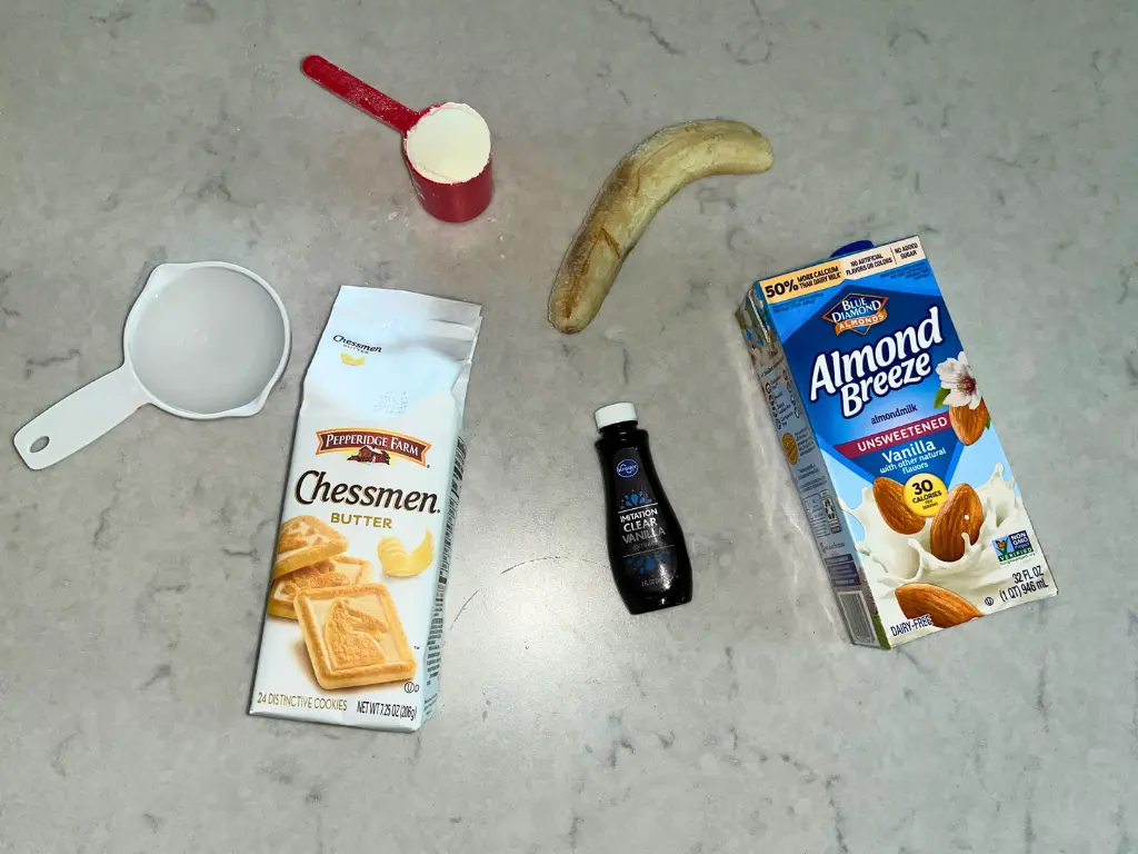 Ingredients for the banana pudding protein shake with Chessmen cookies on a counter.