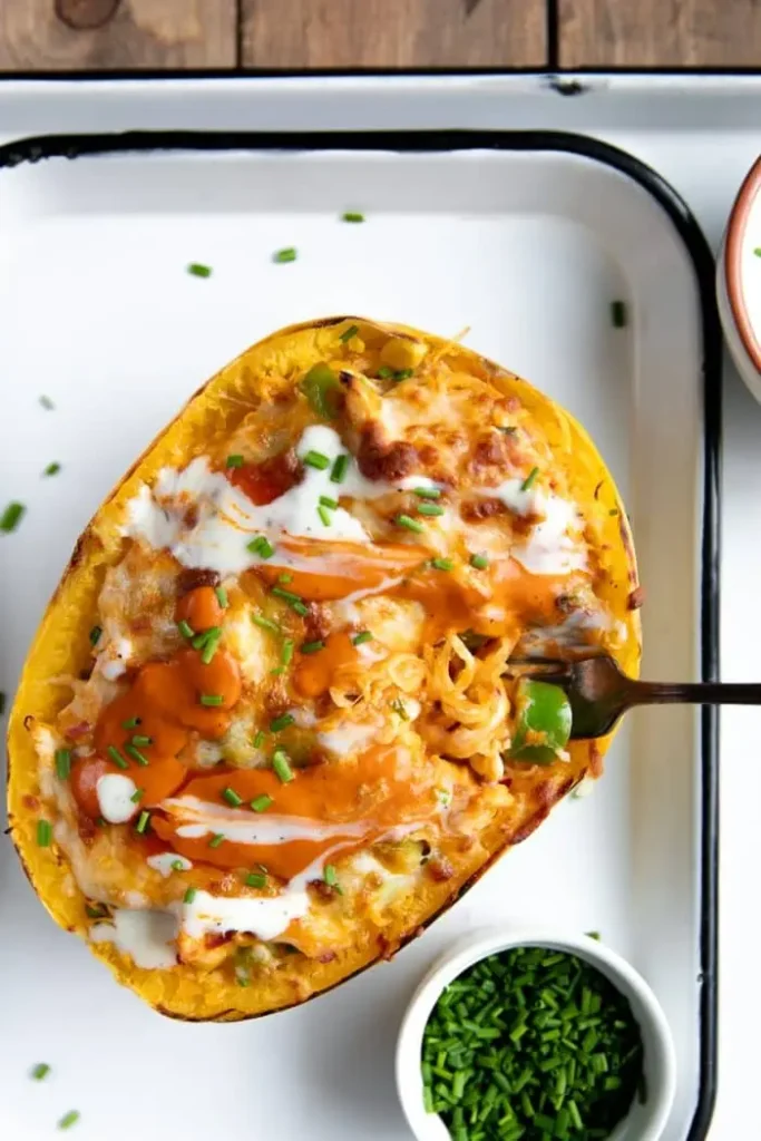 A buffalo chicken stuffed spaghetti squash on a baking sheet with a fork in it.