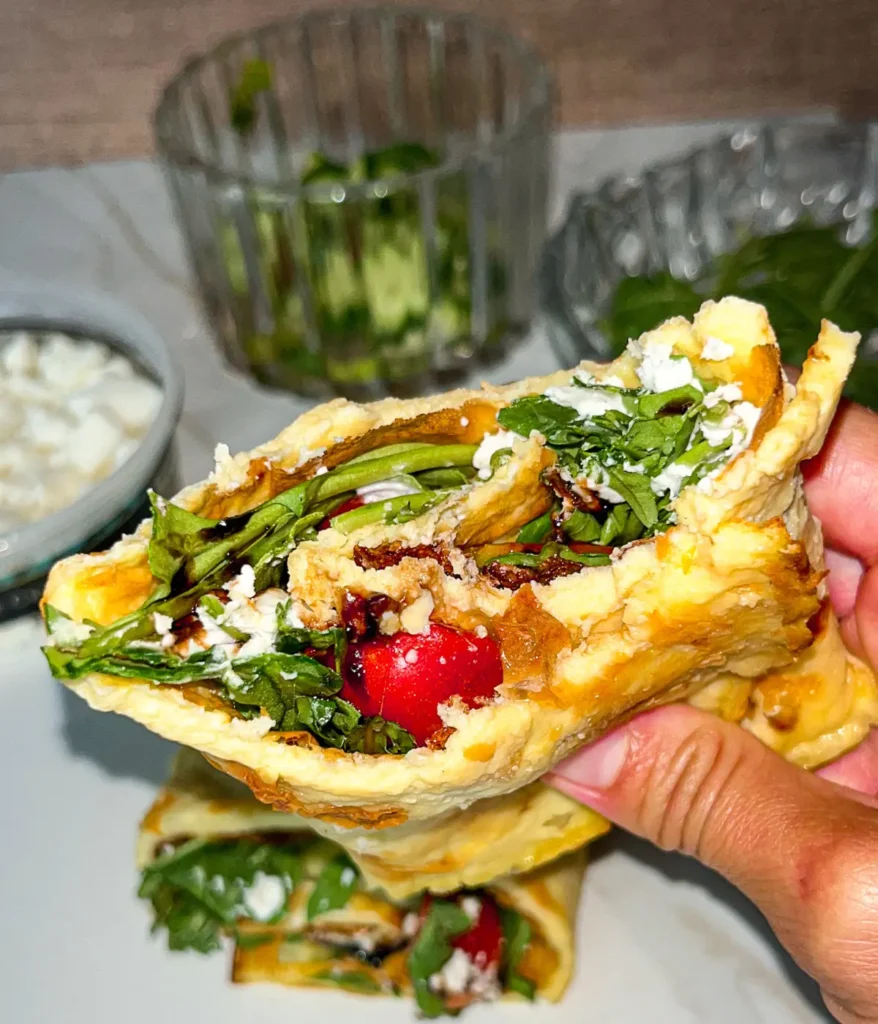 Someone holding a flatbread pita, fully assembled, in their hand after taking a bite.