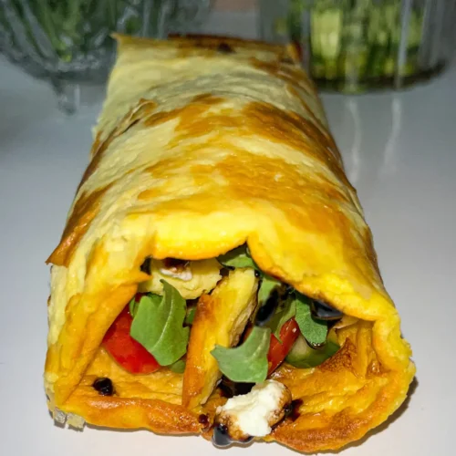 A close-up of a cottage cheese flatbread filled with arugula, goat cheese, and tomatoes on a plate.