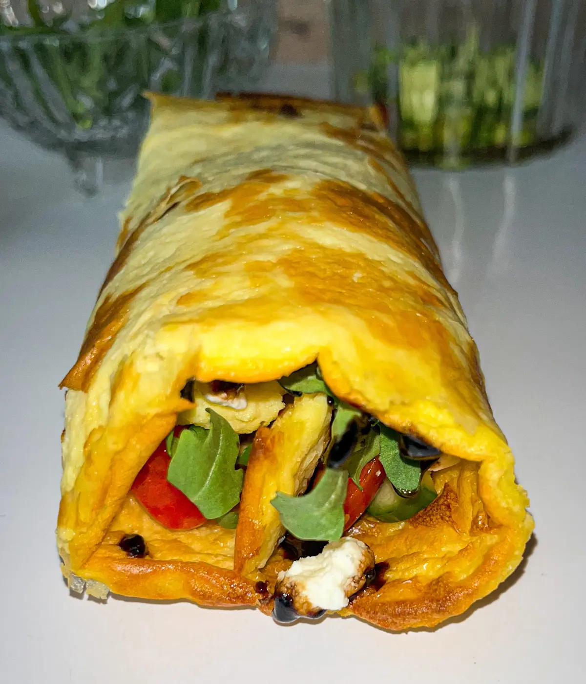 A close-up of a cottage cheese flatbread filled with arugula, goat cheese, and tomatoes on a plate.