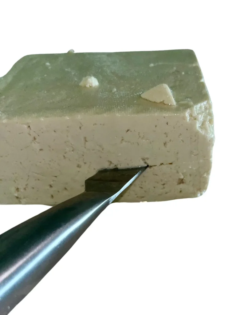 A knife cutting through a tofu block horizontally.