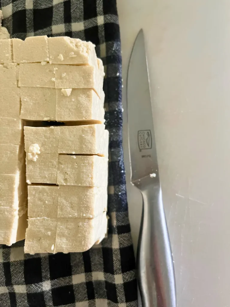 Tofu cut into slices on a towel next to a knife.