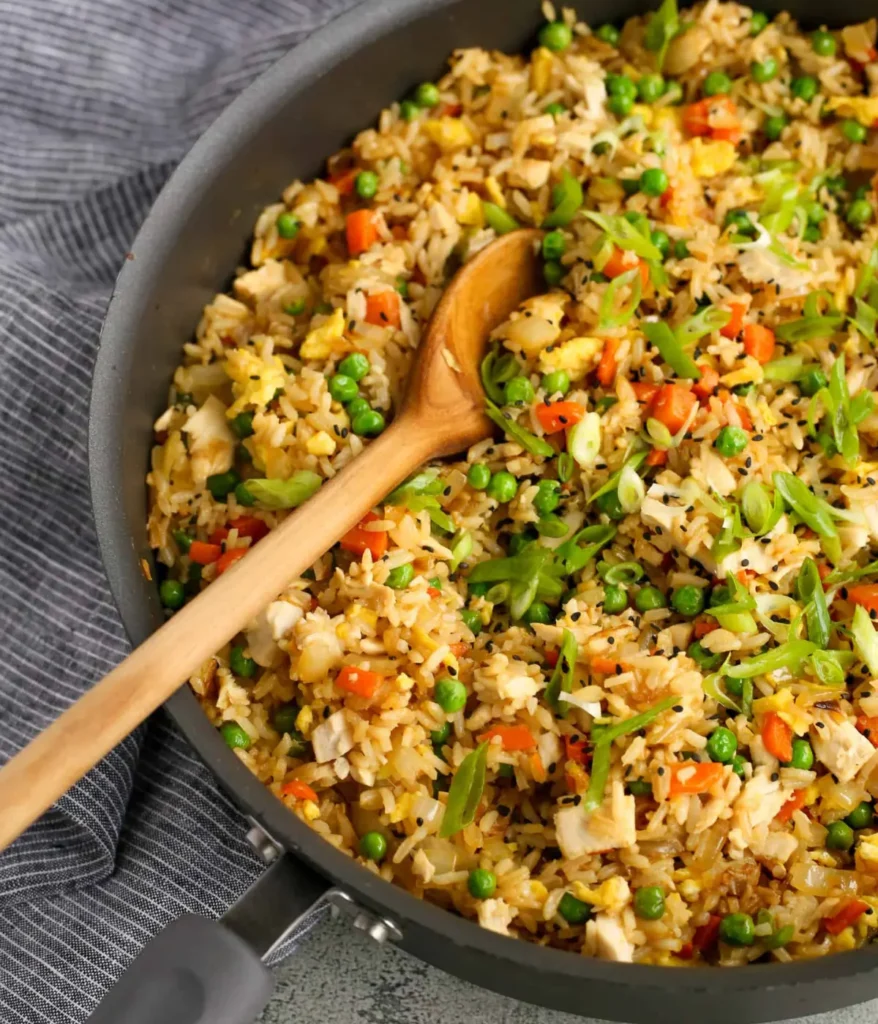 Dairy-free, gluten-free rotisserie chicken fried rice in a pan with a wooden spoon in it.