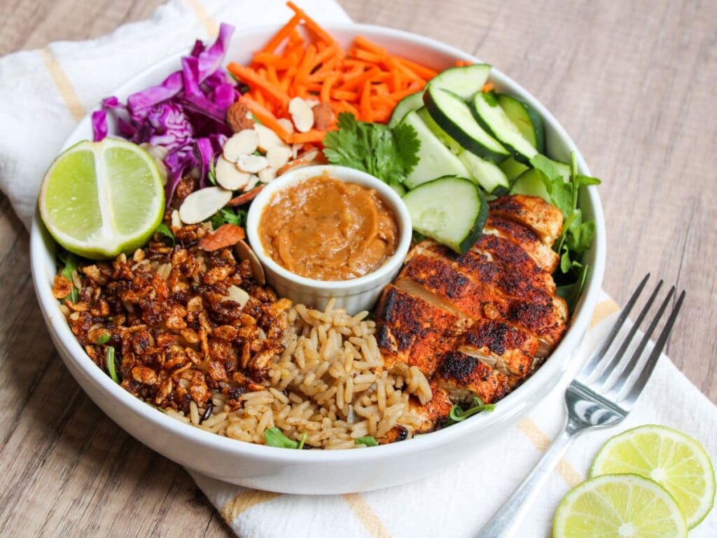 A crispy rice bowl with blackened chicken, fresh veggies, and spicy cashew dressing on a table next to a fork.