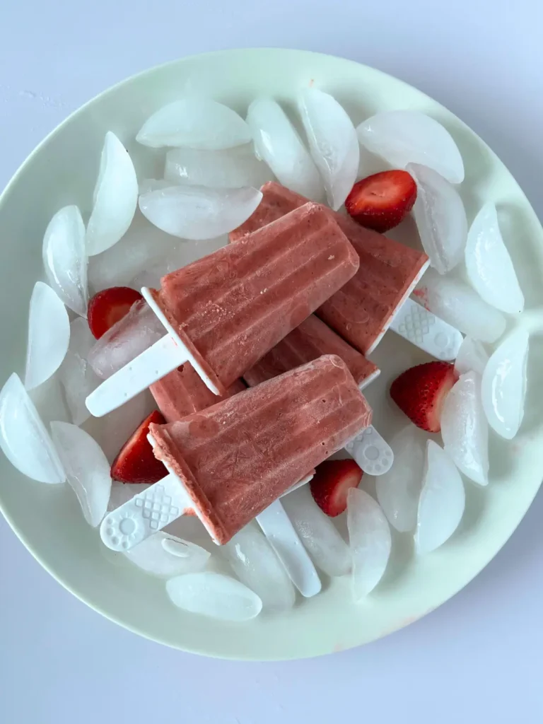 A close-up of strawberry mango popsicles with immune boosting nutrients on a plate with ice and strawberries.