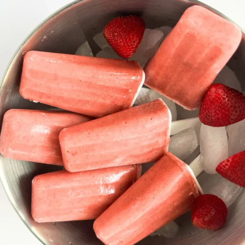A birds-eye view of strawberry mango kefir popsicles in a bowl with ice and strawberries.