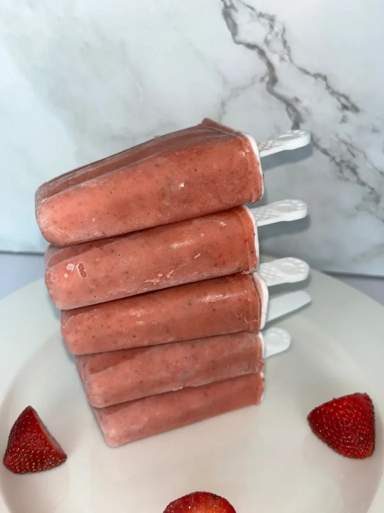 Strawberry mango popsicles stacked on top of each other on a counter.