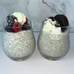 Two kefir chia puddings in glass cups, one topped with berries and whipped cream and the other with Oreos and whipped cream.