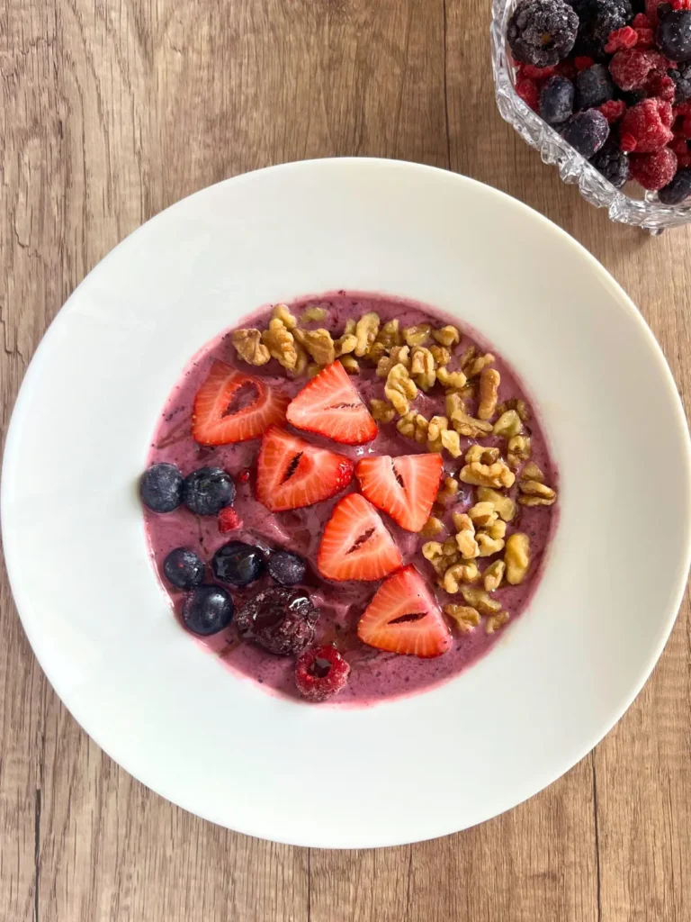 A smoothie bowl topped with walnuts, strawberries and blueberries on a table next to a bowl of berries.