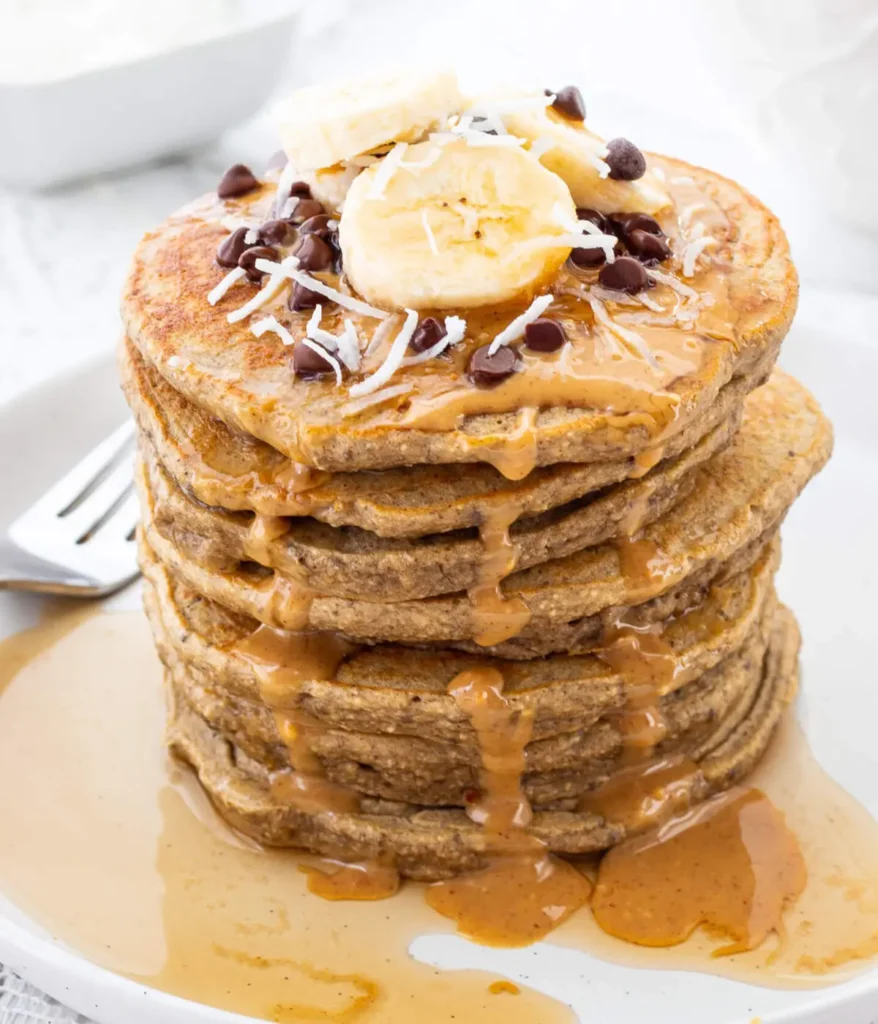 A stack of healthy banana pancakes with mini chocolate chips and banana slices on top on a plate.