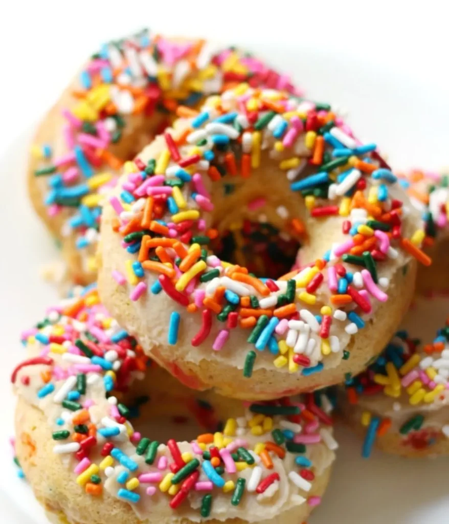 Funfetti protein powder donuts with colorful sprinkles stacked on top of a plate.